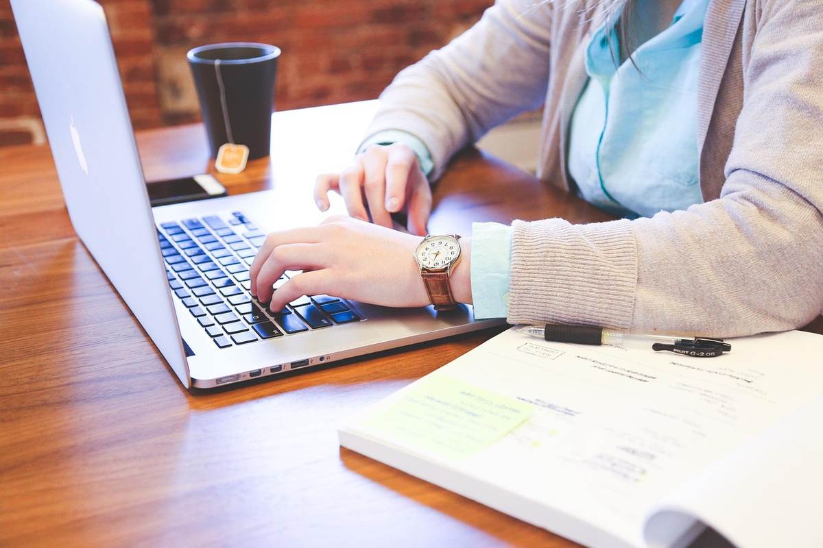 Femme écrivant sur un ordinateur portable avec un livre et une tasse à proximité
