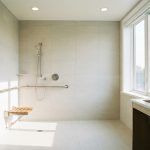 Salle de bain accessible senior, douche de plain-pied avec barre d'appui et siège, carrelage clair, lumineuse