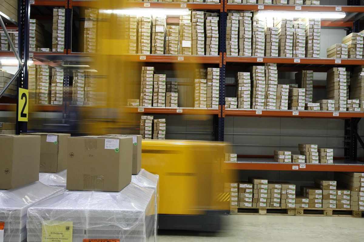 Un chariot élévateur déplace des palettes de cartons dans un entrepôt