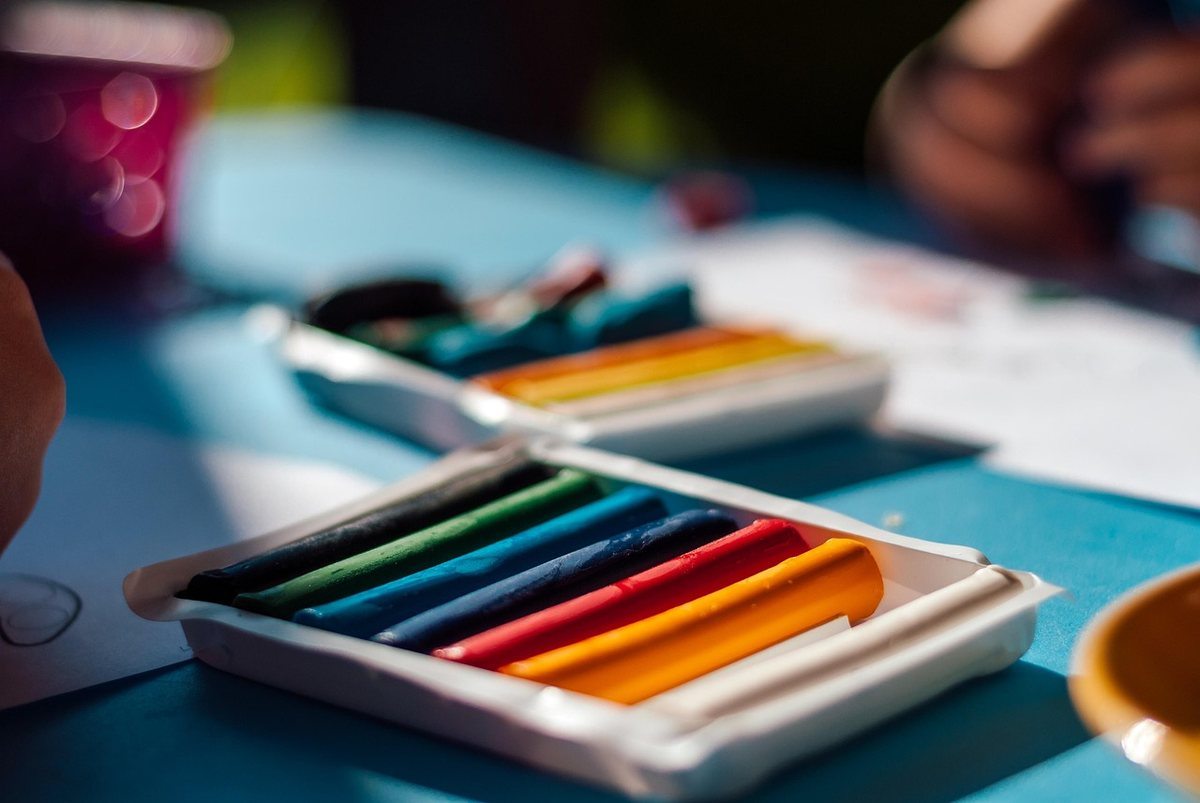 Boîte de crayons de couleur ouverte sur une table avec des feuilles de papier et des matériels de dessin Boîte de crayons de couleur ouverte sur une table avec des feuilles de papier et des matériels de dessin